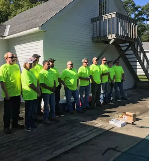 Volunteer crew in matching shirts gathered outside a home under renovation